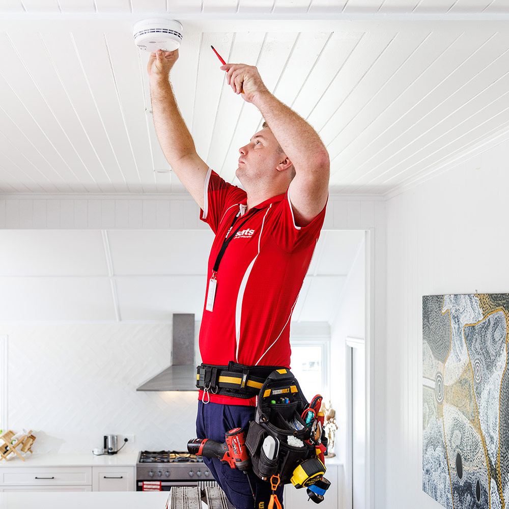 A SATS electrician installing a smoke alarm
